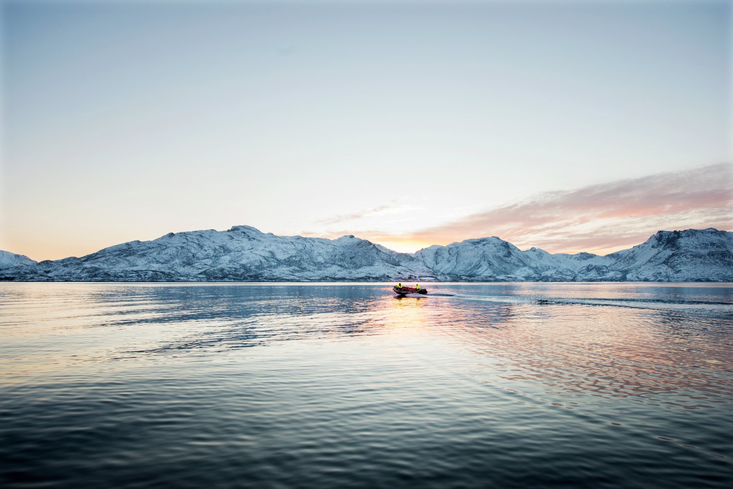 An view of a Norwegian fjord with a salmon farm and snow capped mountains in the distance
