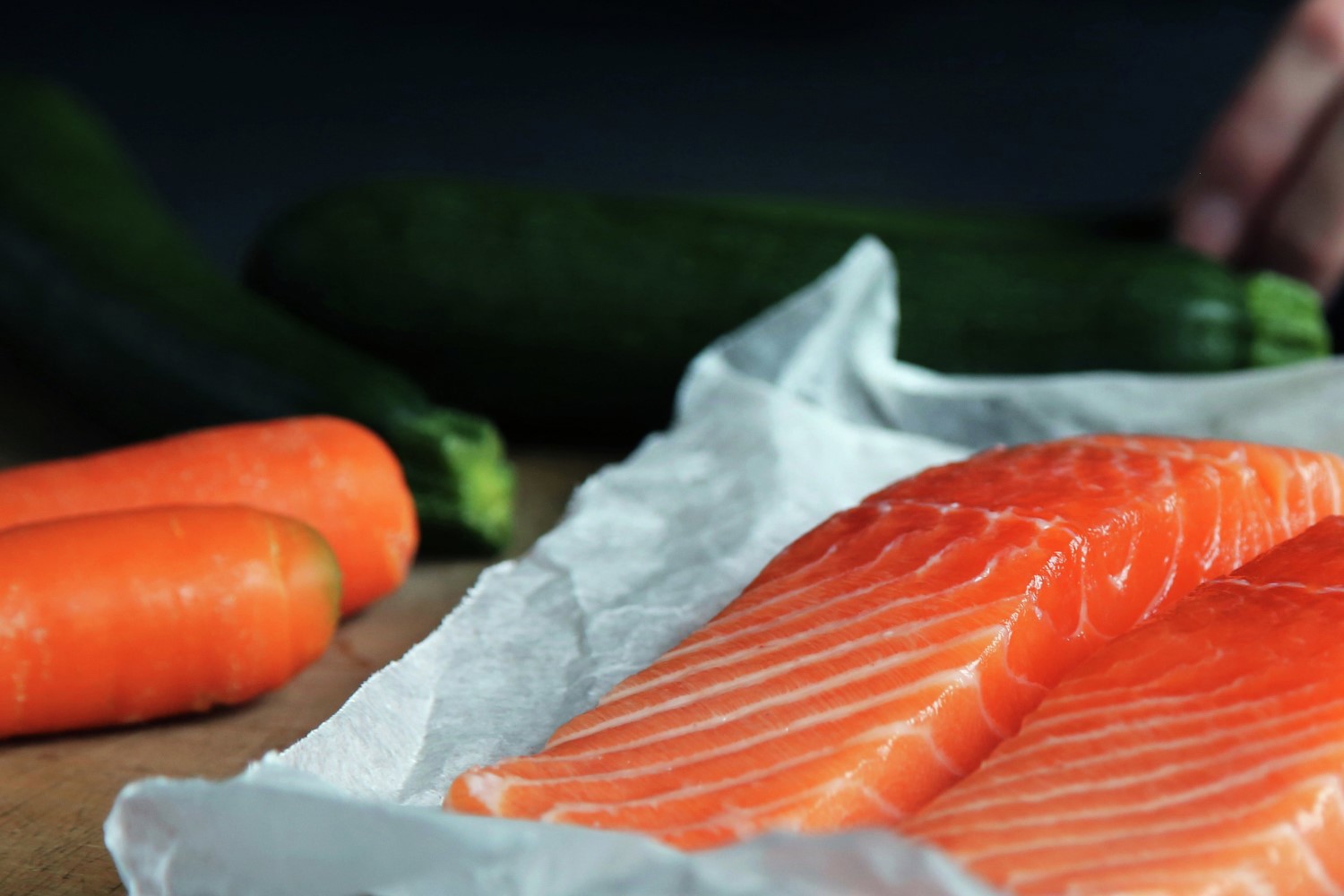 A pciture of salmon fillets on paper with carrots in the background